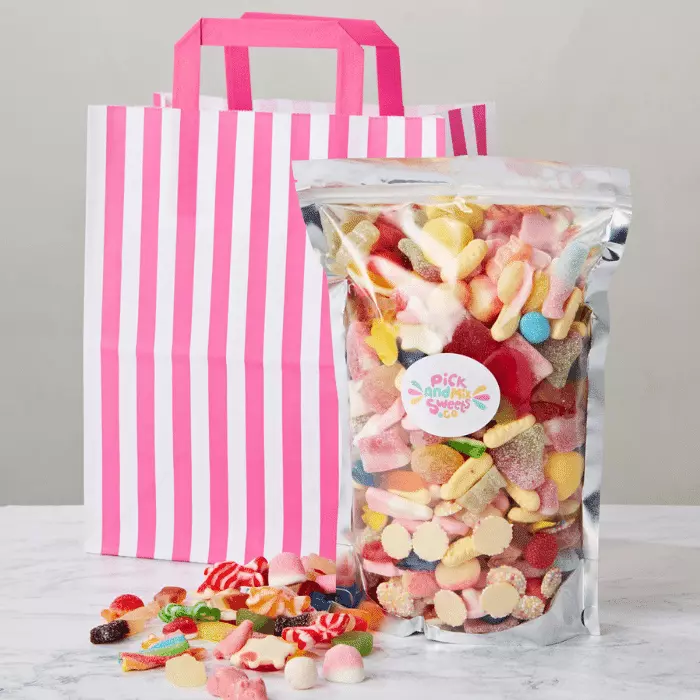 Create Your Own Pick and mix sweets bag filled with sweets in front of pink and white paper bag and pile of sweets.